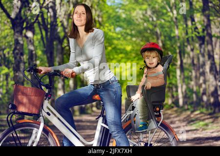 Frau mit einem kleinen blonden Jungen auf dem E-Bike auf dem Rücksitz Stockfoto