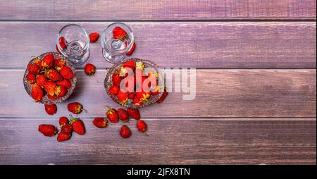 Red ripe strawberries lie in two crystal vases and on wooden table. Nearby are two empty wine glasses. View from above. Stockfoto