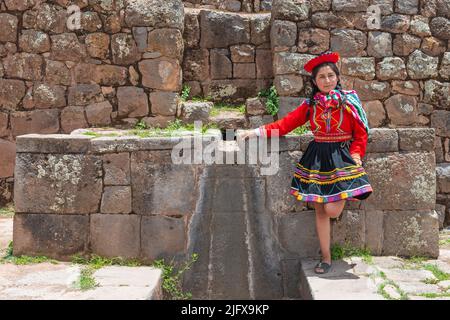 Peruanische indigene Quechua-Frau an einer inka-Mauer mit Brunnen im Heiligen Tal der inka in Tipon bei Cusco, Peru. Stockfoto