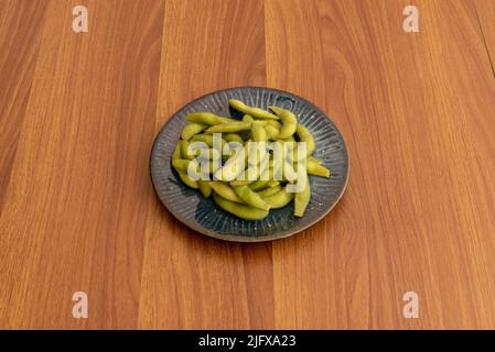 Blauer Teller voller gesalzener Edamame-Schoten auf braunem Holztisch Stockfoto