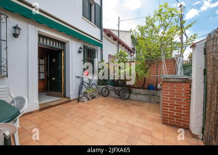 Terrasse eines Einfamilienhauses mit grünem Harz-Tisch und weißen Stühlen, Fahrrad, Haustür und grünen Pflanzen Stockfoto