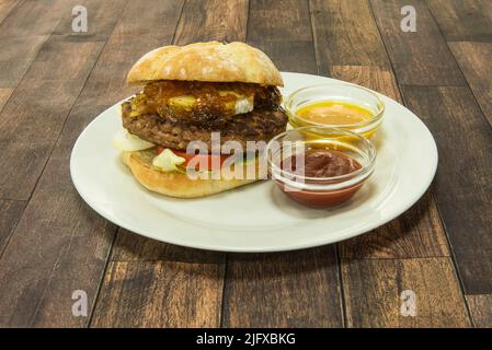 Burger mit Rinderfilet, Ziegenkäse, karamellisierten Zwiebeln, Tomaten und Salat sowie Tomaten- und Senfsoße Stockfoto