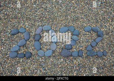 Text 2022 aus schwarzen Steinen auf dem sandigen Hintergrund. Stockfoto