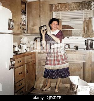 Junge Hausfrau in der Vorstadt in ihrer Küche, die eine Dose Chock Full o' Nuts Kaffee hochhält, um 1950s, USA. Stockfoto