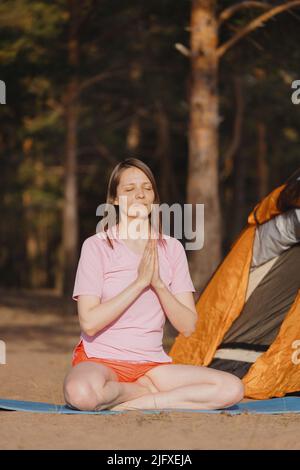 Eine Frau meditiert in der Natur auf einer Yogamatte. Stockfoto