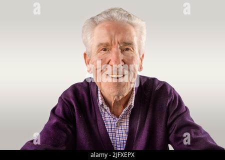 90-jähriger Mann in purpurfarbenem Pullover, der die Kamera glücklich ansieht Stockfoto