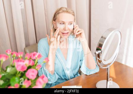 Eine reife Frau mit Augenmaske telefoniert zu Hause. Stockfoto