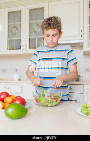 Ein 11-jähriger Junge kocht selbst einen Salat aus Gemüse. Stockfoto