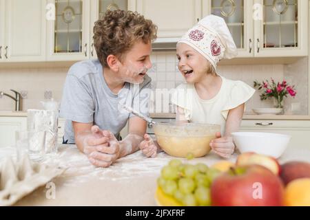 Die Kinder sind alle in Mehl verschmutzt und haben Spaß in der Küche. Stockfoto