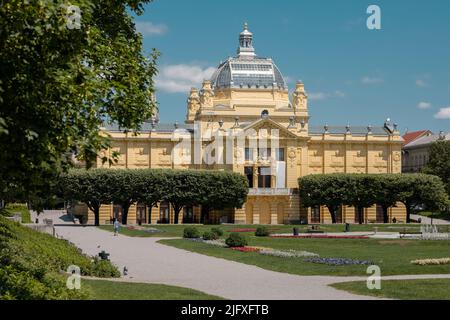 Schönes Gebäude der Kunstgalerie im Zentrum von zagreb am Kralj Tomislav Park an einem heißen Sommertag. Gelbes Gebäude mit roten Blumen im Vordergrund. Stockfoto