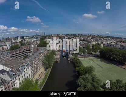 Luftdrohne Panoramablick auf ein Schiff, das über eine aufragende Straßenbrücke im amsterdamer Kanal fährt. Schiff unter offener Brücke über den Kanal. Stockfoto