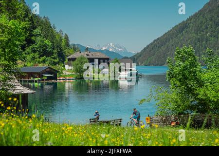 Ostufer oder Südufer am weissensee österreich, schöner Alpensee mit sichtbarem Dorf- und Bootstransport. Radfahrer und Touristen auch sichtbar. Stockfoto