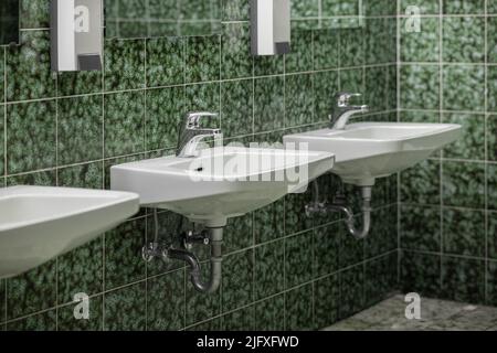 Altes Bad im Vintage-Look mit grünen Fliesen mit Retro-Struktur, weißem Waschbecken und Chrom-Wasserhahn. Stockfoto
