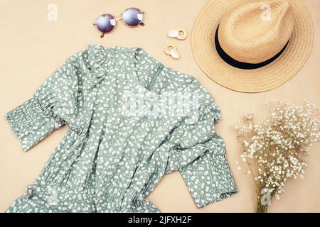 Stilvolle Frauenkleidung und Accessoires. Sommerkleid, Sonnenbrille, Strohhut und Blumenstrauß auf neutralem beigen Hintergrund. Flach liegend, Draufsicht. Stockfoto