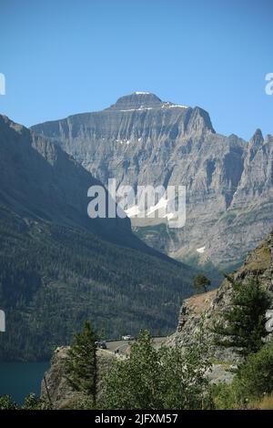 Dramatischer Baum, der an einer Klippe festhält, farbenfroher Little Chief Mountain und Menschen mit Blick auf den St. Mary Lake, strahlend blauer Himmel, Glacier National Park, MT, USA Stockfoto