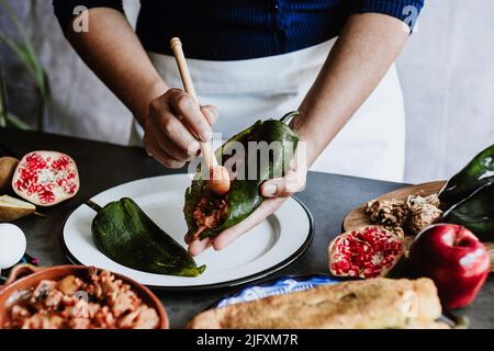 mexikanische Frau Kochen Chiles en nogada Rezept mit Poblano Chili und Zutaten, traditionelles Gericht in Puebla Mexiko Stockfoto