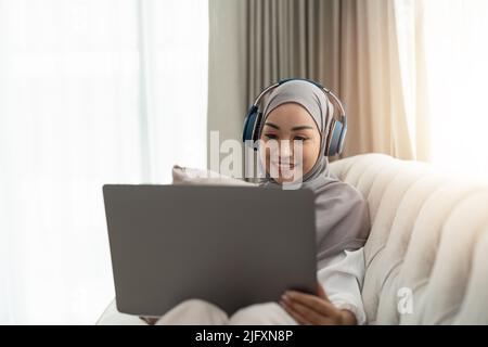 Asiatische muslimische Frau mit Video-Telekonferenz auf ihrem Laptop zu Hause, Online-Lernen oder von zu Hause aus arbeiten Konzept Stockfoto