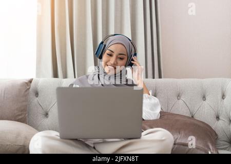 Asiatische muslimische Frau mit Video-Telekonferenz auf ihrem Laptop zu Hause, Online-Lernen oder von zu Hause aus arbeiten Konzept Stockfoto