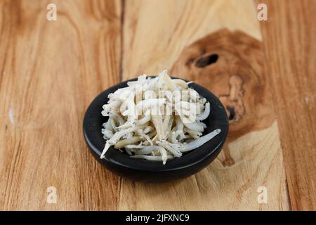 Frisch getrocknete Sardellen auf weißem Hintergrund. Roher, Trocken Gesalzener Meeresfisch. Saltwaterforage Fish. Ikan Asin Teri Medan auf einem Holztisch Stockfoto