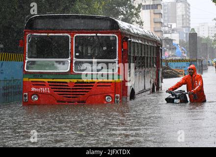 Mumbai, Indien. 05.. Juli 2022. In Mumbai wird ein Mann mit Lebensmittelzustellung gesehen, der sein Fahrrad neben einem BESTEN Bus auf einer überfluteten Straße unter starkem Regen schiebt. In Mumbai regnete es stark, da auf den Straßen Wasser in tief liegenden Gebieten abgeholgt wurde und sich der Verkehr in der Stadt nur langsam bewegte. Das Indian Meteorological Department (IMD) hat in den nächsten 24 Stunden in der Stadt moderate bis schwere Regenfälle vorhergesagt. Kredit: SOPA Images Limited/Alamy Live Nachrichten Stockfoto