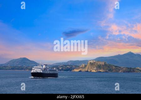 Italien, landschaftlich schöner Sonnenuntergang über Procida Island bei Neapel mit einem Boot, das sich aus der Ferne nähert. Stockfoto