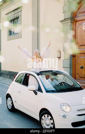 Die Braut lehnte sich mit den Händen nach oben in den Kofferraum des Fiat 500 Stockfoto