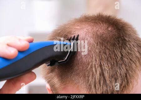 Ein Mann schneidet sich mit einem Haarschneider die Haare. Schneiden einer kurzen Frisur zu Hause. Nahaufnahme. Stockfoto