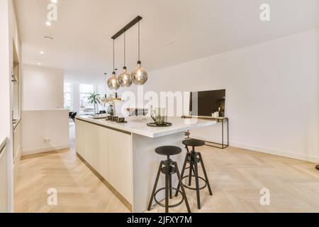 Offene Küche mit dunkelweißen Schränken und Pendelleuchten in luxuriösem Apartment Stockfoto