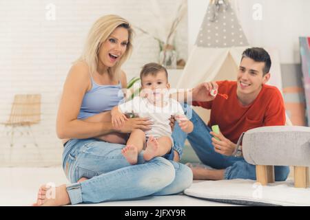 Glückliche kaukasische Familie spielt mit Seifenblasen im Wohnzimmer, Full-Shot-Familie und Wohlbefinden Konzept. Hochwertige Fotos Stockfoto