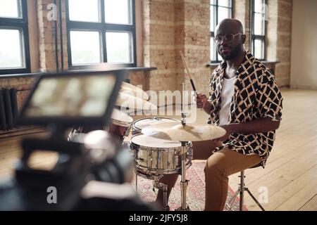 Porträt eines jungen afrikanischen Schlagzeugers, der vor der Kamera am Schlagzeug für die Online-Übertragung im leeren Studio auftrat Stockfoto