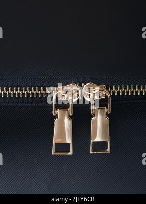 goldene Reißverschlüsse mit goldenen Reißverschlüssen sind auf einem schwarzen Lederobjekt aus der Nähe befestigt Stockfoto