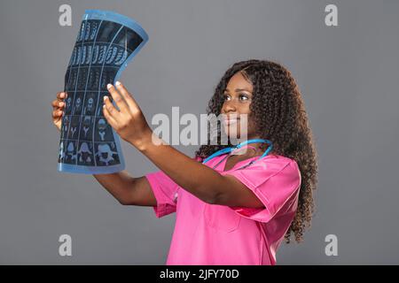 Porträt eines intelligenten afroamerikanischen medizinischen Personals mit weißem Mantel und Blick auf Röntgenaufnahmen, CT und MRT Stockfoto