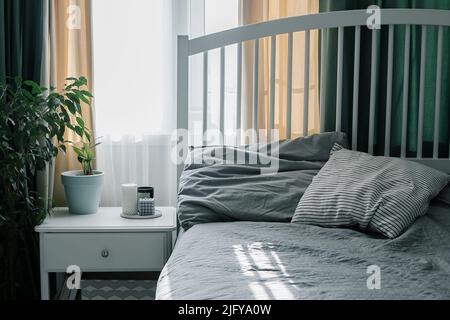 Schlafzimmer mit heller Innenausstattung. Moderne Kerze, Hauspflanze auf Nachttisch neben dem Bett. Lifestyle zu Hause. Stockfoto