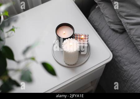 Luxuriöse Duftkerze im Schlafzimmer auf dem Betttisch. Home gemütliche Innenausstattung. Draufsicht Stockfoto