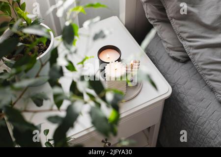 Moderne brennende Kerze auf dem Nachttisch neben dem Bett. Raumduft-Dekor-Konzept. Wellness. Stockfoto