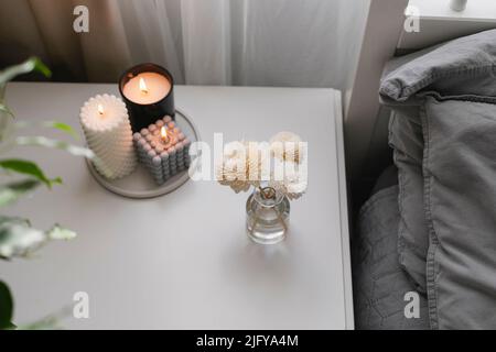 Aromatischer Reed-Lufterfrischer und brennende Kerze auf dem Nachttisch im Schlafzimmer. Nach Hause duftendes Aroma. Wellness, Wohlbefinden Stockfoto