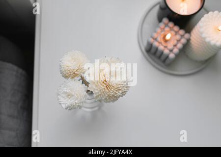 Aromatischer Reed-Lufterfrischer und brennende Kerze auf dem Nachttisch im Schlafzimmer. Nach Hause duftendes Aroma. Wellness. Stockfoto