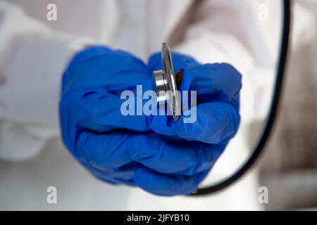 Die Hände des Arztes in blauen Handschuhen, die ein Stethoskop halten. Nahaufnahme. Die Hände des Arztes tragen Einweghandschuhe mit Stethoskop. Stockfoto
