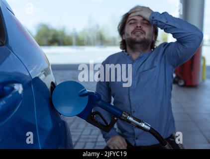 Tanken eines Autos mit Benzin an einer Tankstelle. Anstieg der Kraftstoffpreise. Krise und Mangel an Benzin. Ein Mann schreit vor Wut in der Nähe der Tankstelle Stockfoto