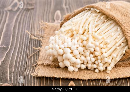 Weißer frischer goldener Nadelpilz oder Enoki-Pilz im Sack auf braunem Holzbrett Hintergrund Stockfoto
