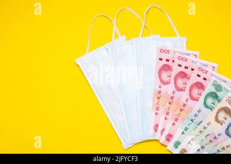 Chinesische Banknote (Yuan) und neue weiße Maske auf gelbem Hintergrund. Maske ist wichtig, aber Mangel und sehr teuer in vielen Ländern der Virus-Situation in Stockfoto