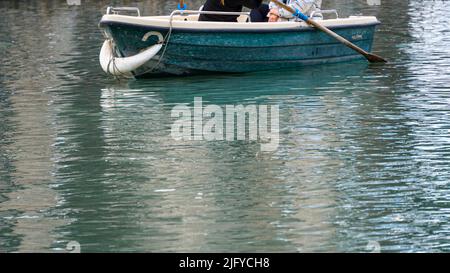 Bild von zwei Personen in einem kleinen blauen und alten Boot. Menschen paddeln in einem kleinen Boot auf einem See mit sauberem Wasser. Stockfoto