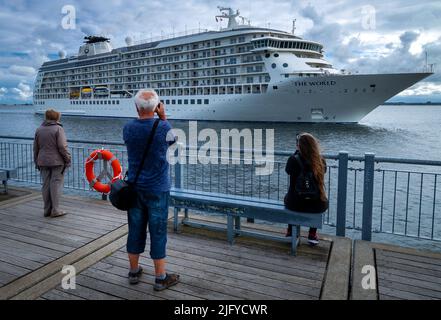 Wismar, Deutschland. 06.. Juli 2022. Passanten beobachten vom Pier aus, wie der Luxusliner „The World“ den Hafen erreicht. Auf dem 196 Meter langen Schiff leben mehr als 100 Familien aus 20 Nationen in ihren Privatwohnungen und reisen gemeinsam um die Welt. Quelle: Jens Büttner/dpa/Alamy Live News Stockfoto