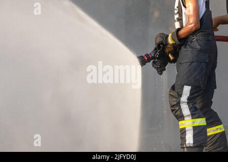 Feuerwehrmann oder Feuerwehrmann sprühen Wasser aus einem großen Wasserschlauch, um ein Feuer zu verhindern Stockfoto