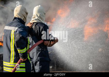 Feuerwehrmann oder Feuerwehrmann sprühen Wasser aus einem großen Wasserschlauch, um ein Feuer zu verhindern Stockfoto