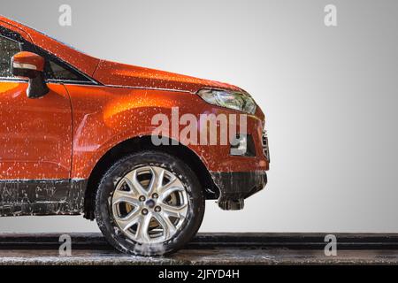 Oranges Auto mit weißer Seife auf der Karosserie in der Autowerkstatt. Konzentrieren Sie sich auf den Außenspiegel. Isoliert auf grauem Hintergrund Stockfoto