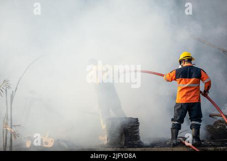 Feuerwehrmann oder Feuerwehrmann sprühen Wasser aus einem großen Wasserschlauch, um ein Feuer zu verhindern Stockfoto