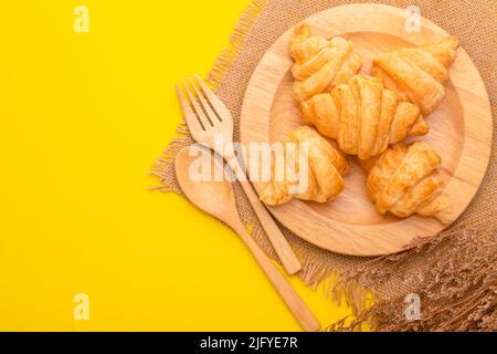 Draufsicht Mini Croissant in Holzschale auf gelbem Hintergrund. Food-Konzept mit Kopierraum Stockfoto