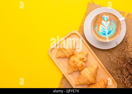 Draufsicht Mini Croissant in Holzschale und Kaffee auf gelbem Hintergrund. Food-Konzept mit Kopierraum Stockfoto