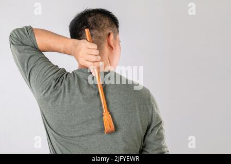 Health Care oder Juckreiz oder Tinea cruris Konzept : Porträt von Menschen mit kratzenden Holz Stick Scratch auf seiner Rückseite. Studio auf grauem Backgro gedreht Stockfoto